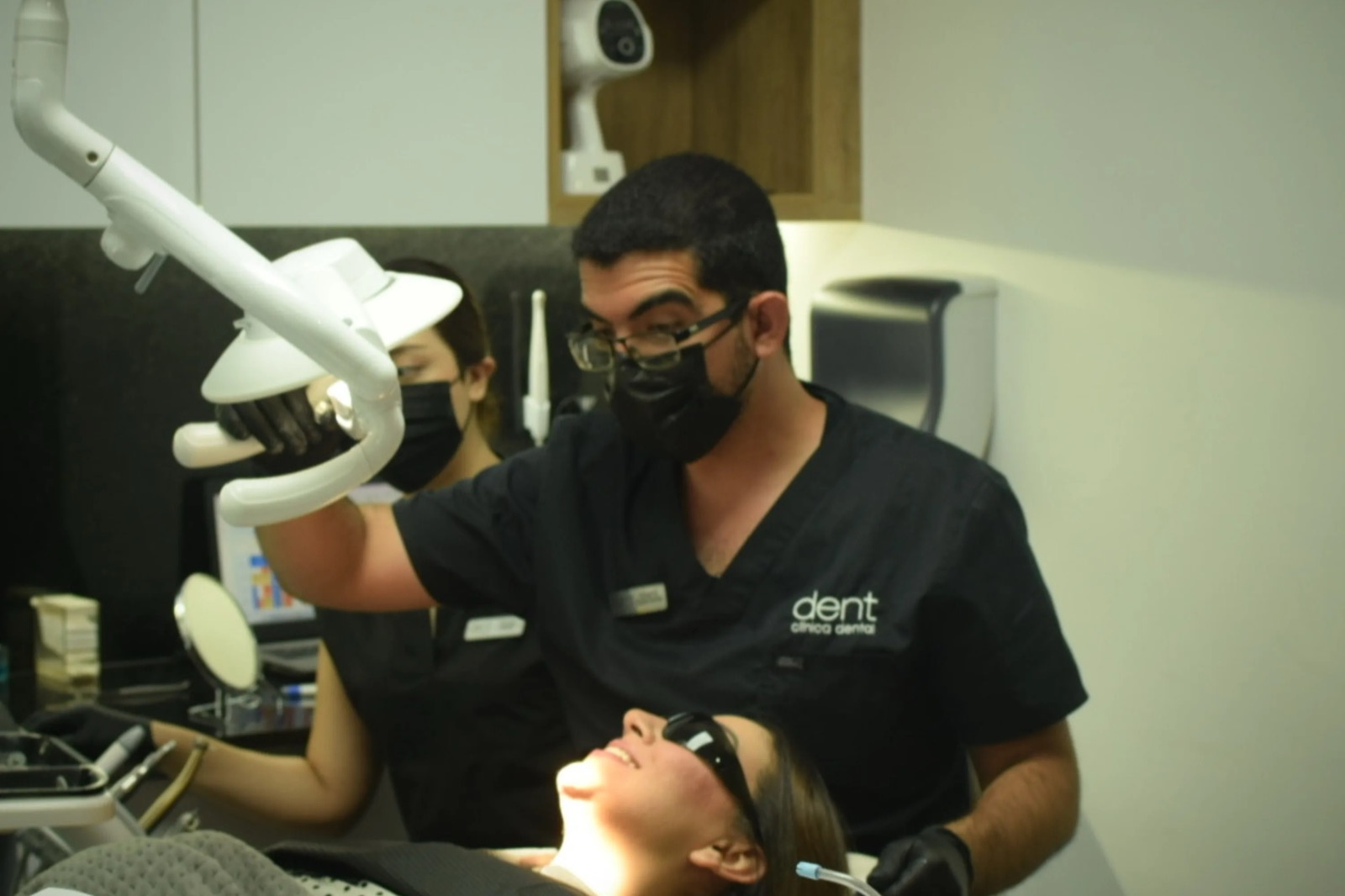 Especialista de dent clínica dental coloca la lámpara sobre una paciente en el sillón, acompañado de su asistente