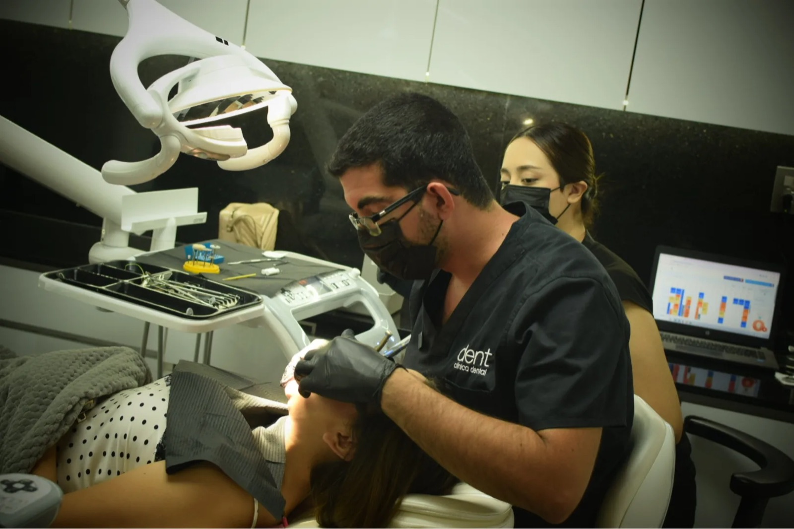 Especialista de Dent Clínica Dental atiende a una paciente en el sillón del consultorio junto a su asistente