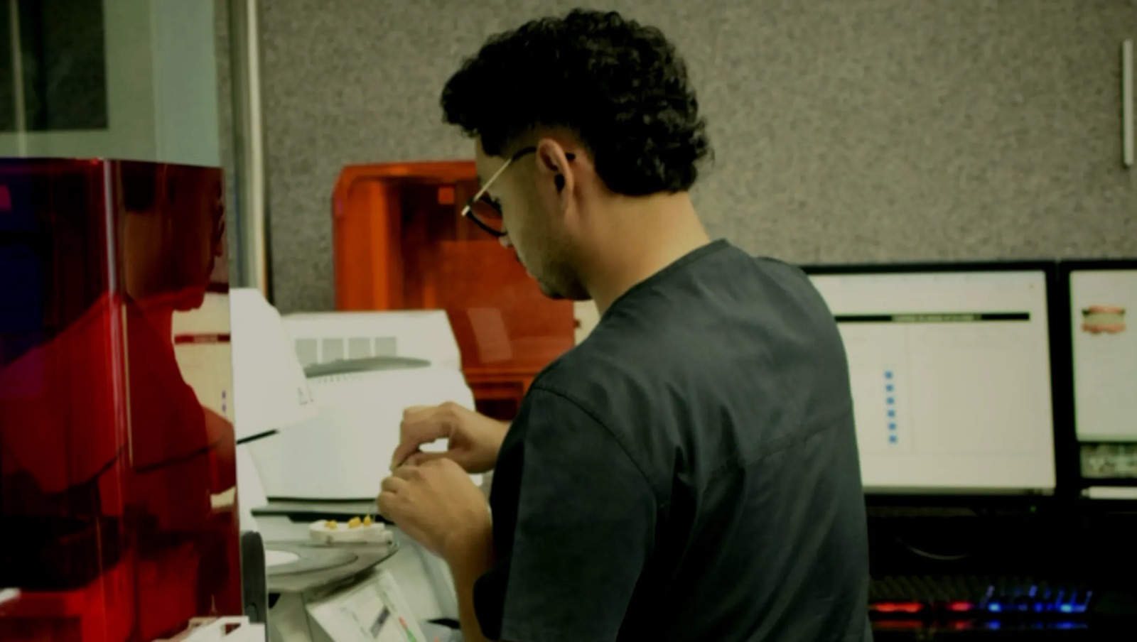 Técnico de Dent Lab trabajando junto a las impresoras de resina del laboratorio, con el caso abierto en las pantallas