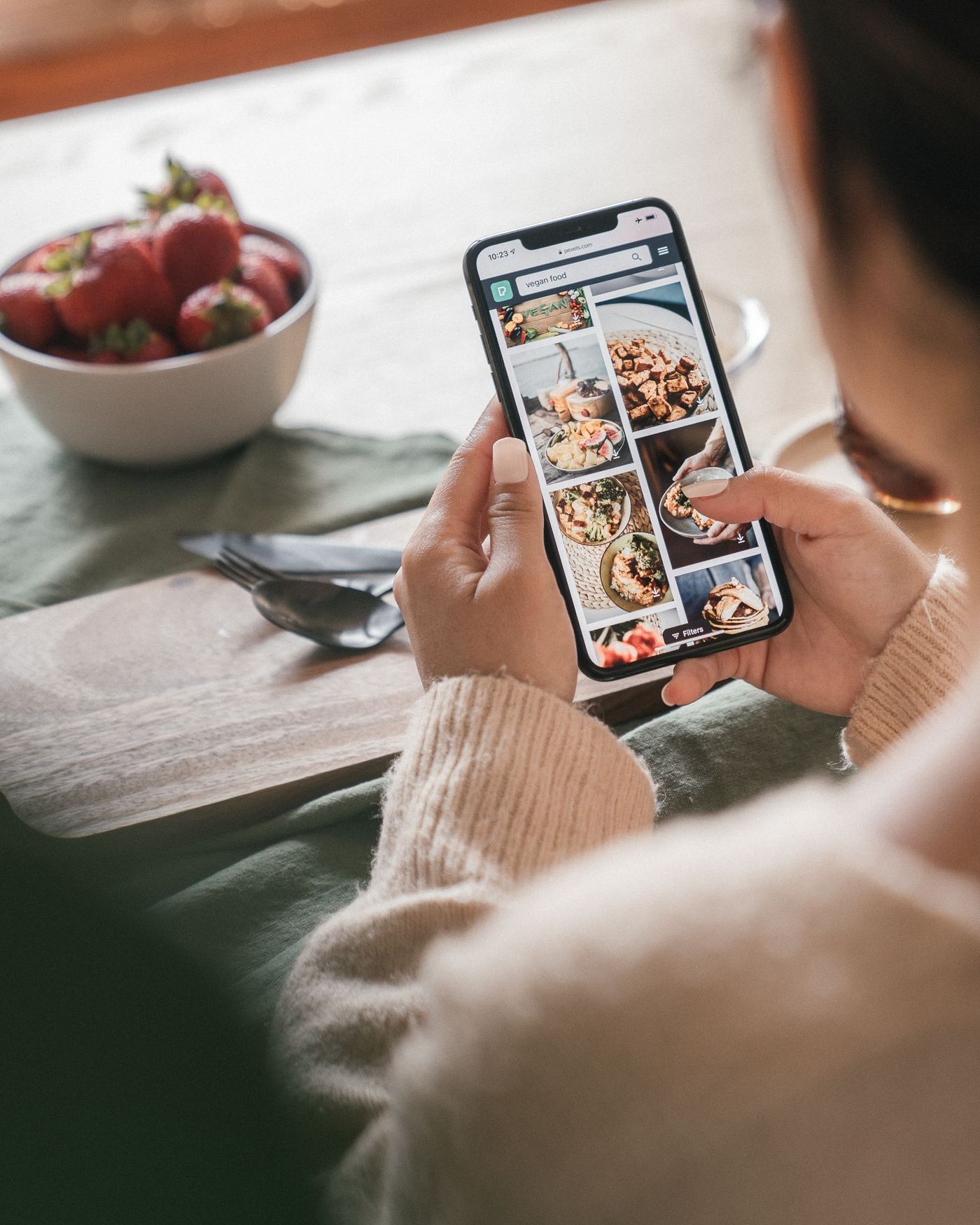 Persona revisando una página web en su celular, sentada a la mesa durante el desayuno